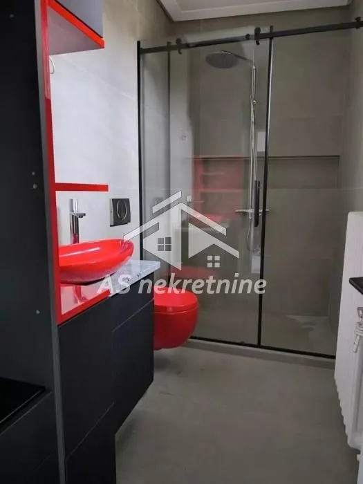 Moderno opremljeno kupatilo sa tuš kabinom i crvenim sanitarijama.