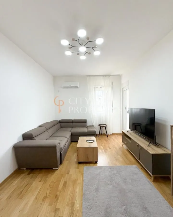 Living room with a sectional sofa, TV, and wooden flooring.