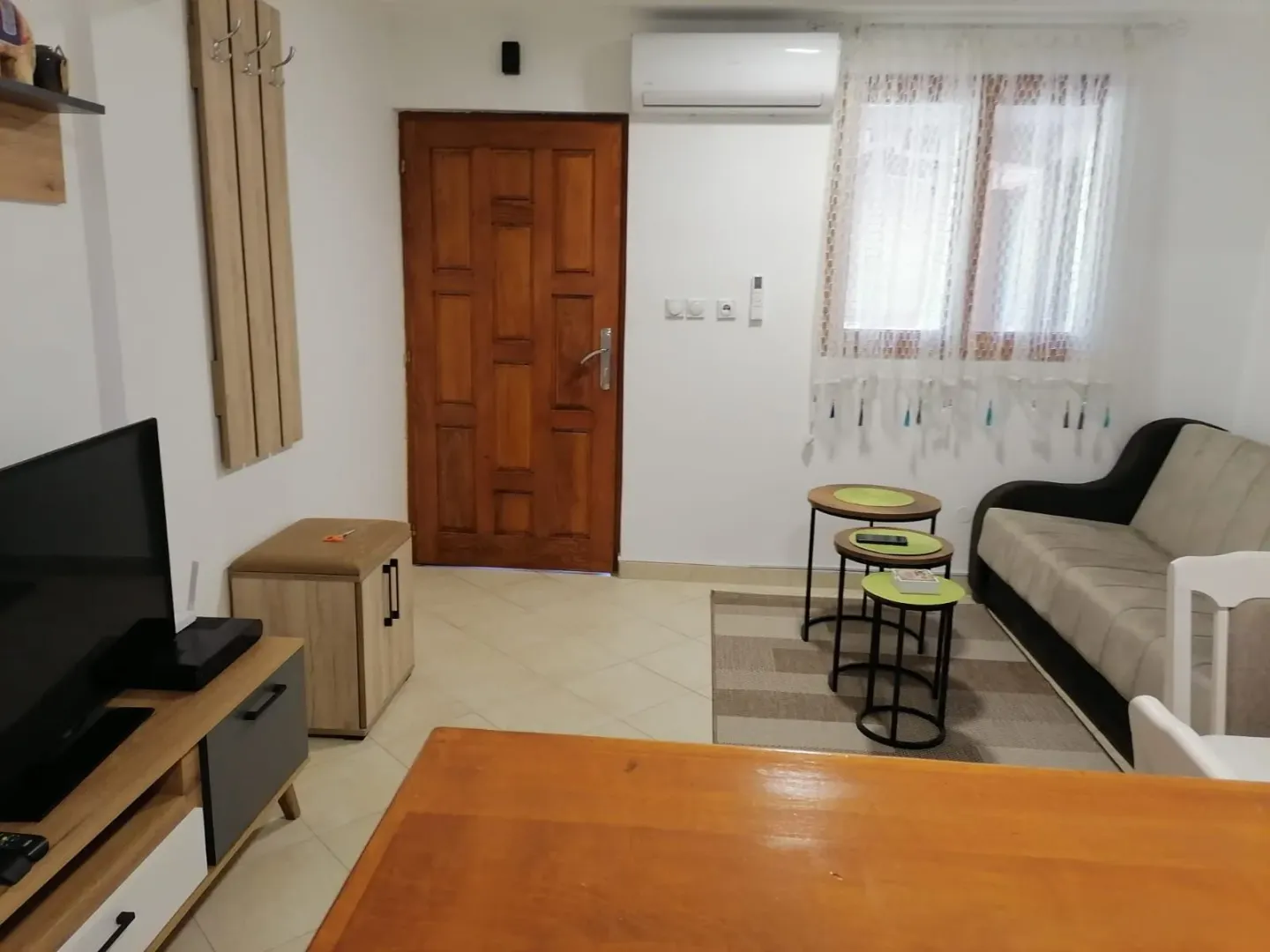 Manja dnevna soba sa garniturom, televizorom i drvenim ulaznim vratima.