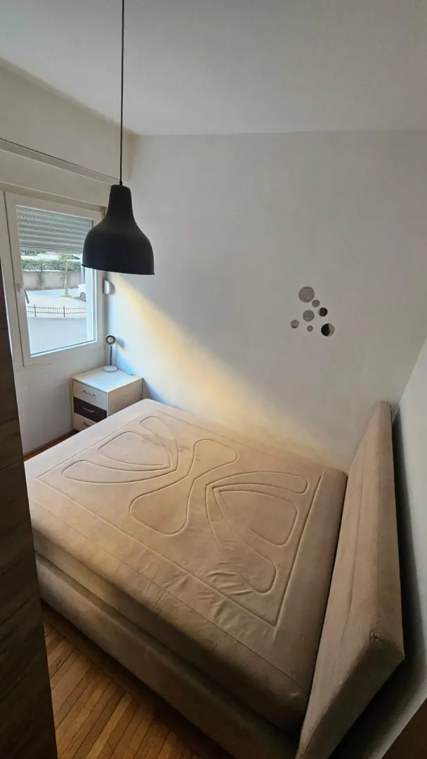 Manja spavaća soba sa bračnim krevetom, noćnim stočićem i prozorom.