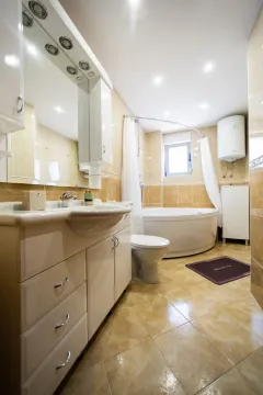 Kupatilo opremljeno umivaonikom, ugaonom kadom, wc šoljom i elementima u bež tonovima. - image 13