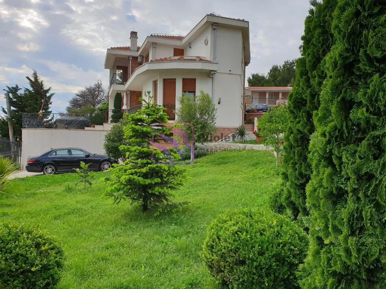 Pogled na dvorište i fasadu porodične kuće sa uređenim travnjakom i zelenilom.