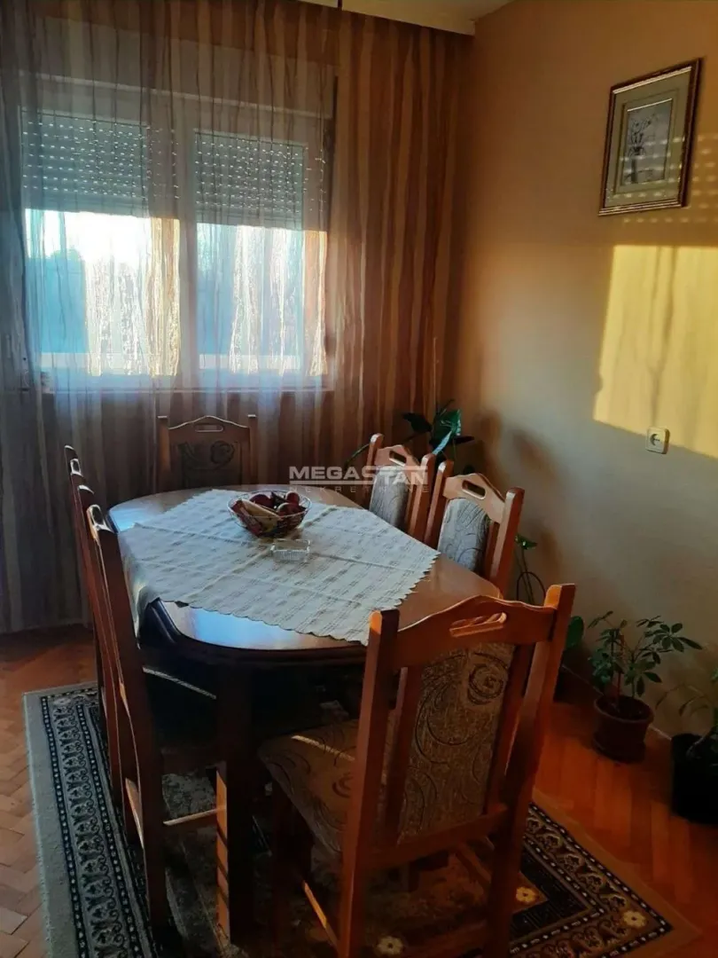 Trpezarija sa drvenim stolom i stolicama pored prozora.