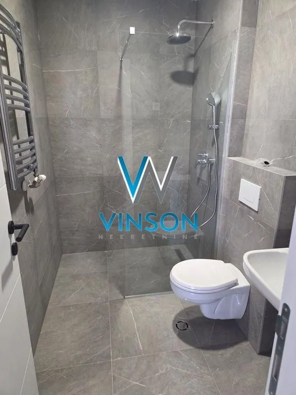 Modernly equipped bathroom with a walk-in shower and grey tiling.