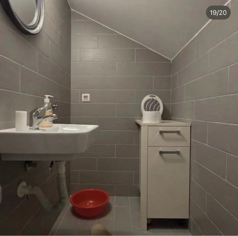 Small bathroom with grey tiles, a sink, and a white cabinet.