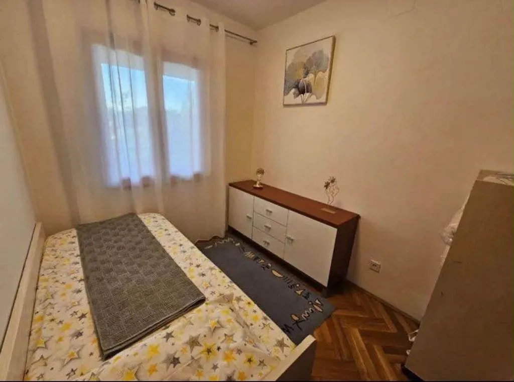 Manja spavaća soba sa krevetom, komodom i prozorom.