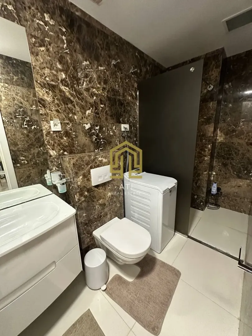 Moderne kupatilo sa mermernim pločicama, wc šoljom, umivaonikom i mašinom za veš.