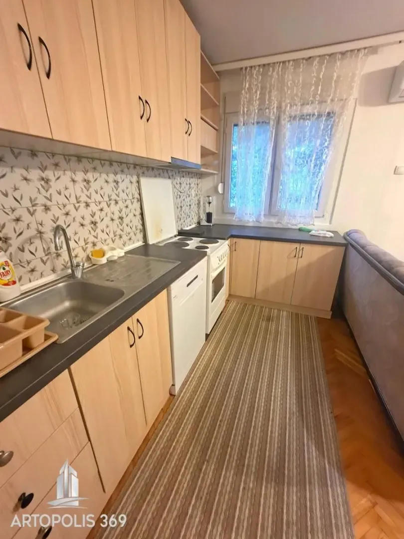 Manja kuhinja sa drvenim elementima i sudoperom pored prozora.
