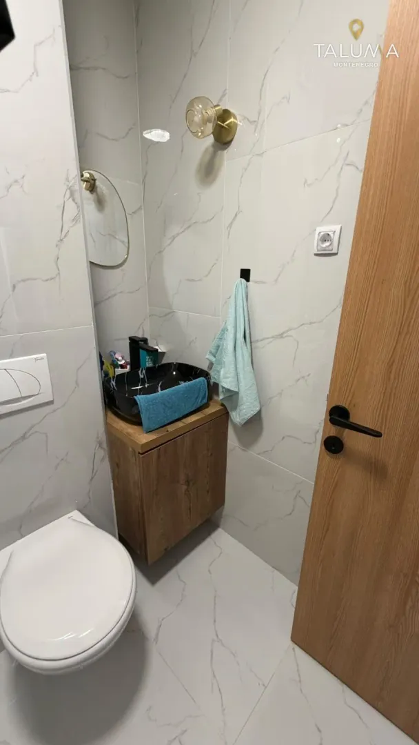 Small bathroom lined with marble tiles featuring a washbasin and a toilet.