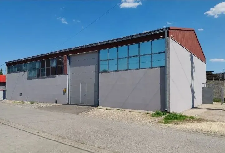 Exterior view of a modern warehouse building with large windows and an asphalt driveway.
