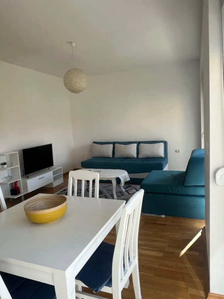 Dnevna soba sa garniturom, TV-om i trpezarijskim stolom.