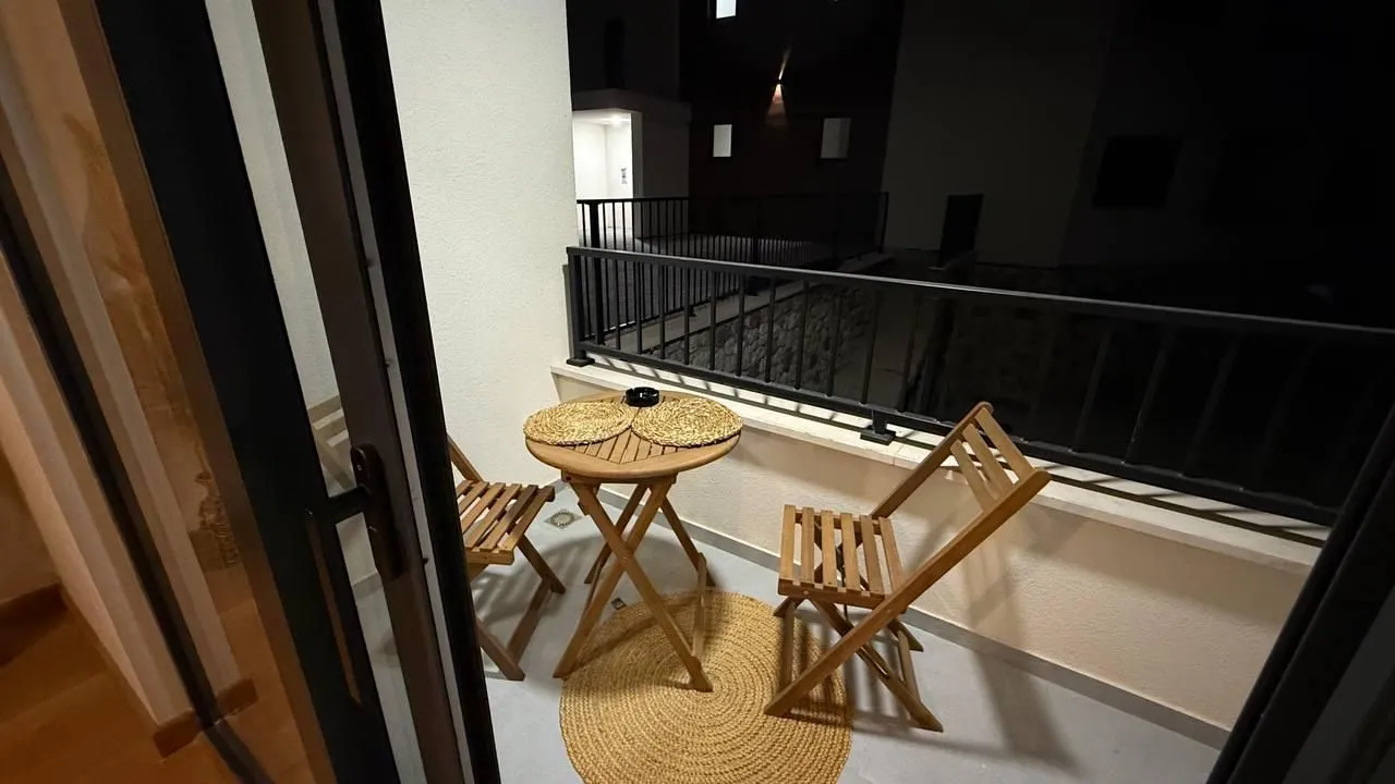 Manji namješteni balkon sa drvenim stolom i stolicama noću.