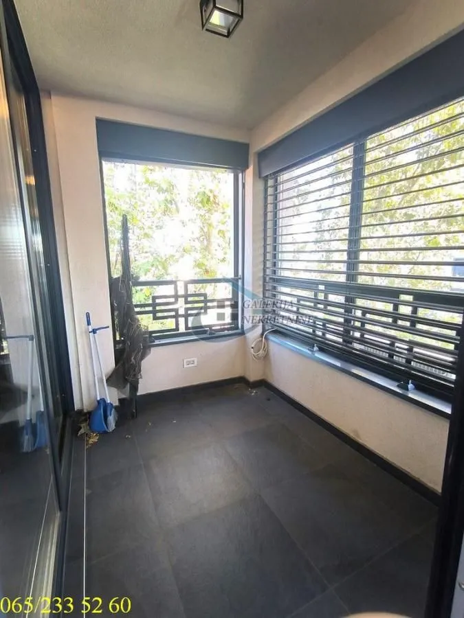 Zastakljeni zatvoreni balkon sa velikim prozorima i tamnim podnim pločicama.