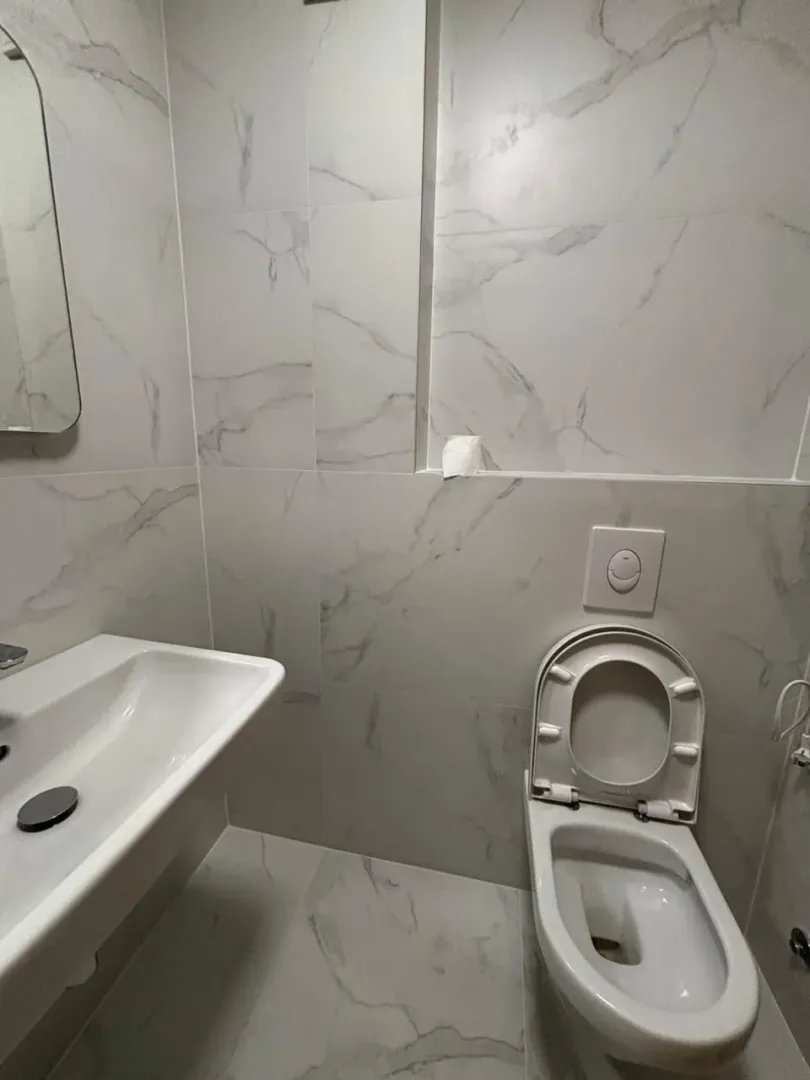 Moderne opremljeno kupatilo sa bijelim mermernim pločicama, umivaonikom i toaletom.