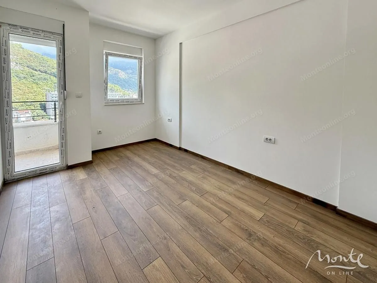 Prazna soba sa drvenim podom i izlazom na balkon.