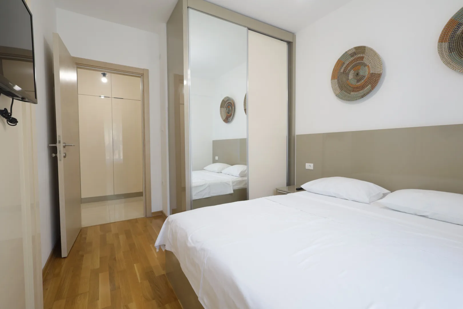 Bright bedroom with a double bed, a large mirrored wardrobe, and an open door leading to the hallway.