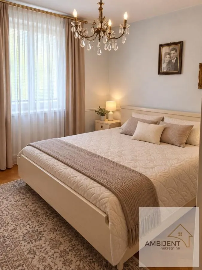 Nameštena spavaća soba sa bračnim krevetom, prozorom i lusterom.