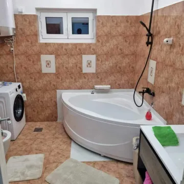 Kupatilo sa ugaonom kadom, umivaonikom, veš mašinom i smeđim keramičkim pločicama. - image 5
