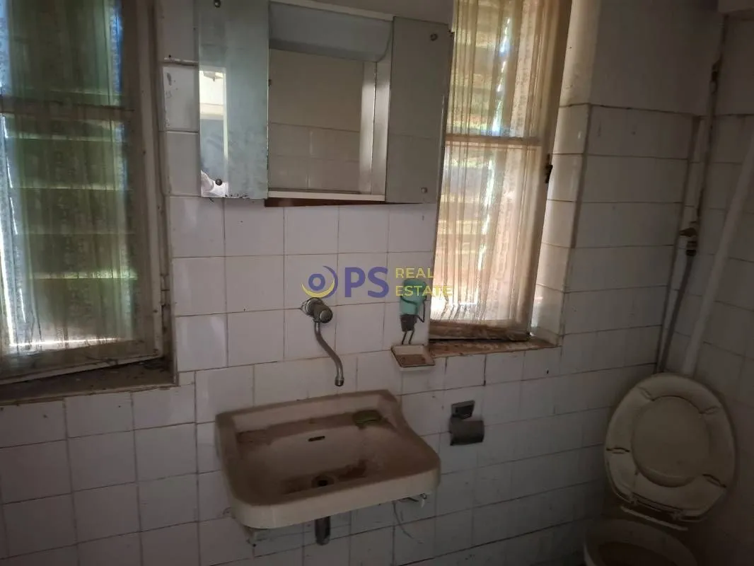 Starije kupatilo sa umivaonikom, ogledalom i toalet šoljom.