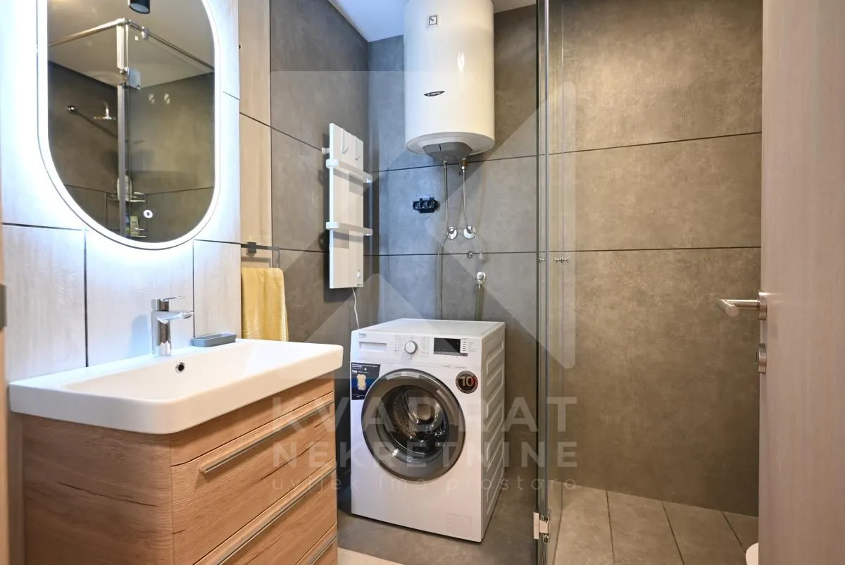 Modernly equipped bathroom with a washbasin, walk-in shower, and washing machine.