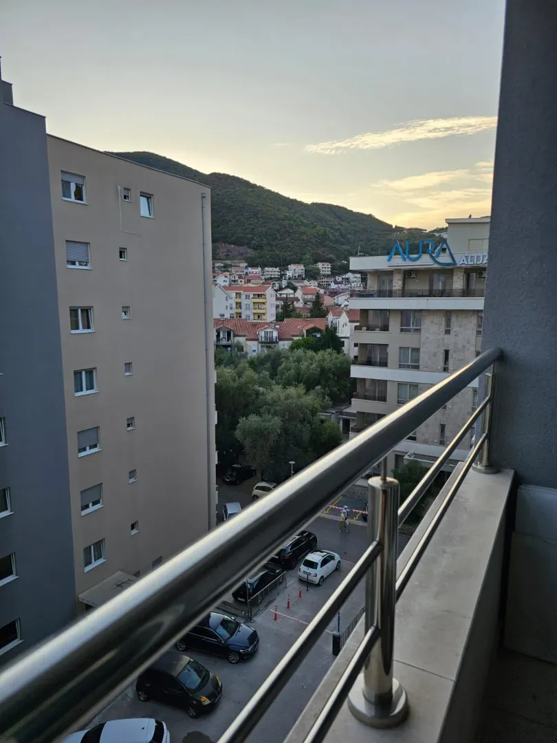 Pogled sa balkona na okolne zgrade i brdo.