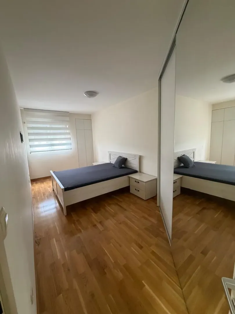 Spavaća soba sa bračnim krevetom, noćnim stočićem i ugradnim ormarom sa ogledalom.