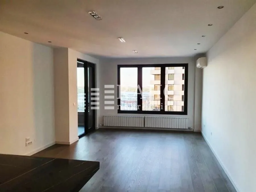 Spacious empty living room with large windows and hardwood flooring.