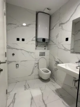 Moderno opremljeno kupatilo sa bijelim mermernim pločicama, wc šoljom, umivaonikom i bojlerom. - image 6