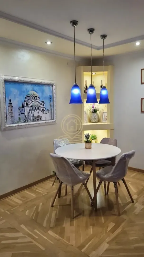 Trpezarija sa okruglim stolom, modernim stolicama i dekorativnim osvetljenjem.