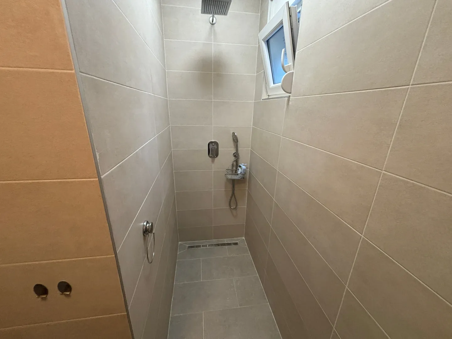 Modern shower cabin lined with beige tiles and a built-in shower faucet.