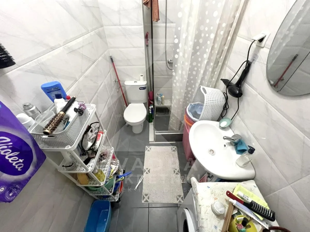 Manje kupatilo sa tuš kabinom, umivaonikom, WC šoljom i policama za odlaganje.