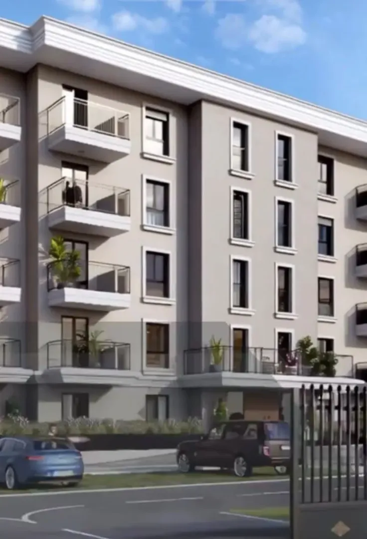 Spoljašnji izgled moderne stambene zgrade sa balkonom i uređenim dvorištem.