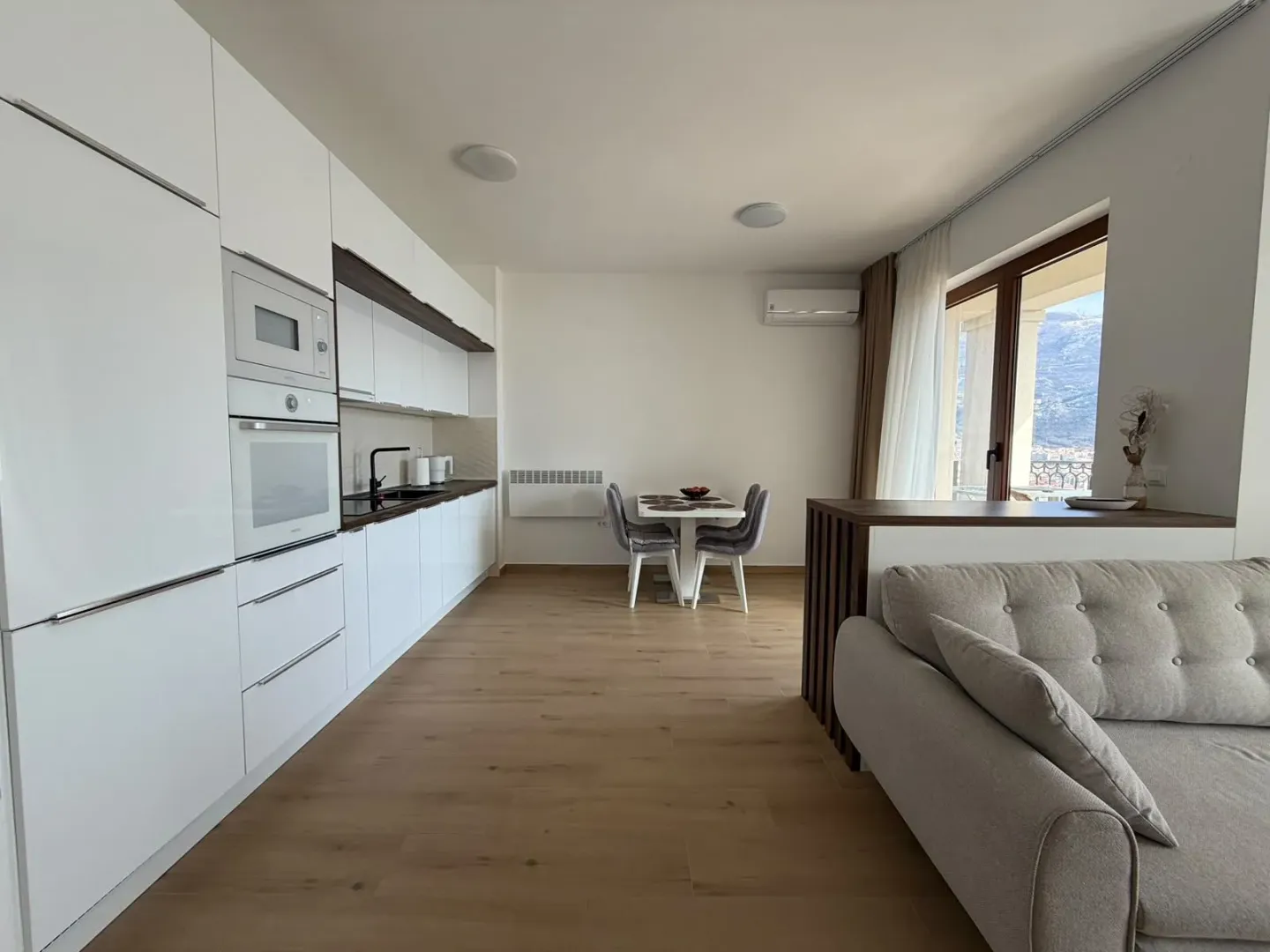 Moderna bijela kuhinja sa trpezarijom i izlazom na terasu.