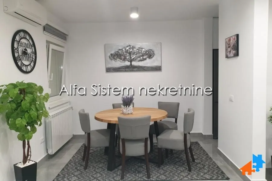Trpezarija sa okruglim drvenim stolom i sivim tapaciranim stolicama.