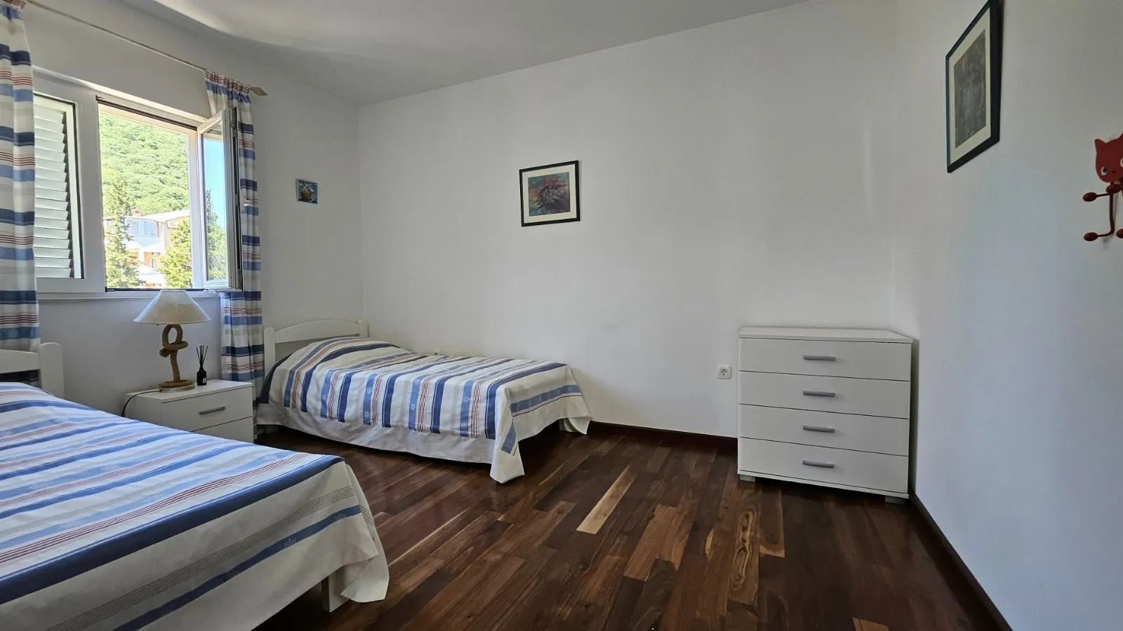 Spavaća soba sa dva kreveta, komodom i prozorom.