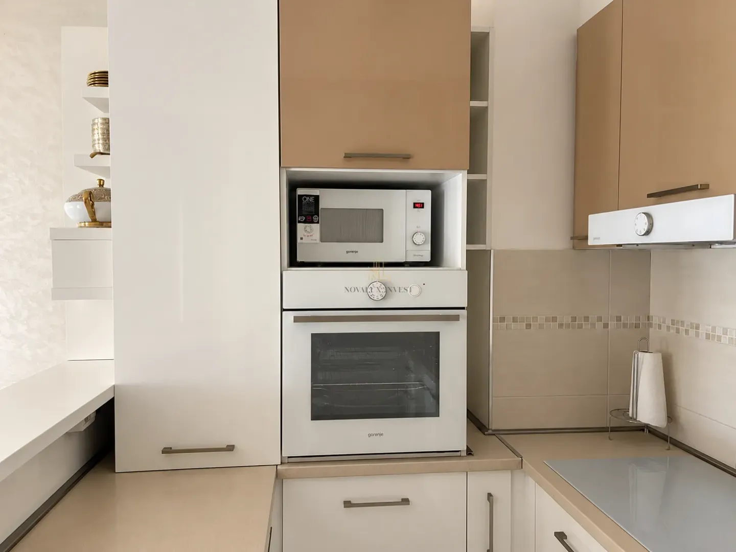 Kuhinja sa ugradnom rernom, mikrotalasnom pećnicom i gornjim elementima u bež tonovima.