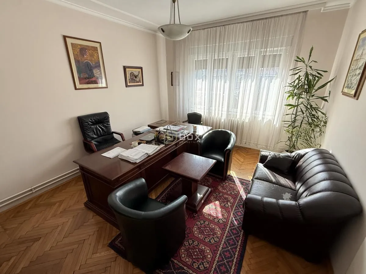 Radna soba opremljena velikim drvenim radnim stolom, crnim kožnim foteljama i garniturom.