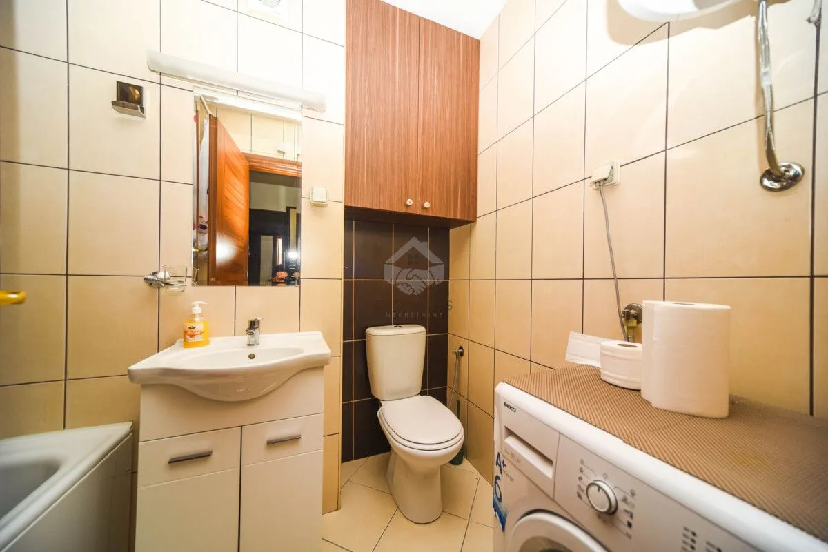 Kupatilo opremljeno umivaonikom, WC šoljom, ormarićem i veš mašinom.