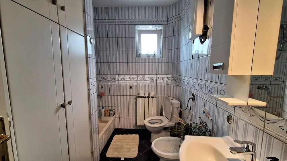Kupatilo sa pločicama, umivaonikom, toaletom i ugradnim ormarom.