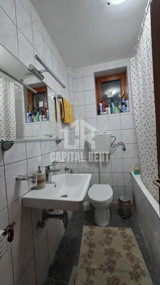 Manje kupatilo obloženo keramičkim pločicama sa umivaonikom, WC šoljom i tuš kabinom.