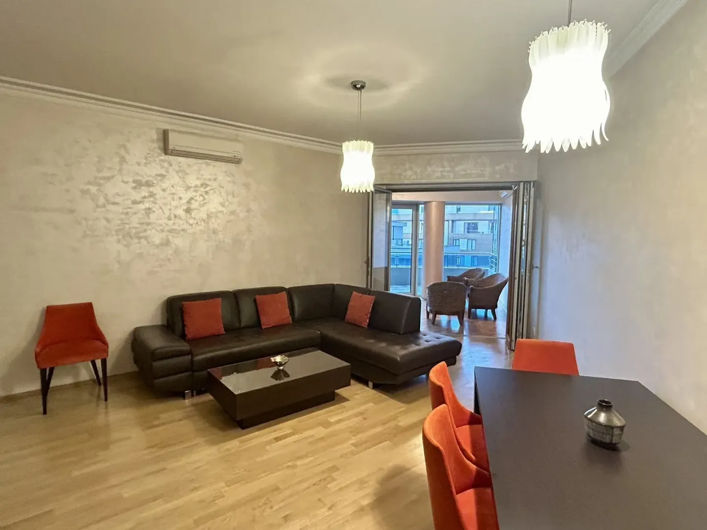 Bright living room with a dark leather corner sofa and a dining table.