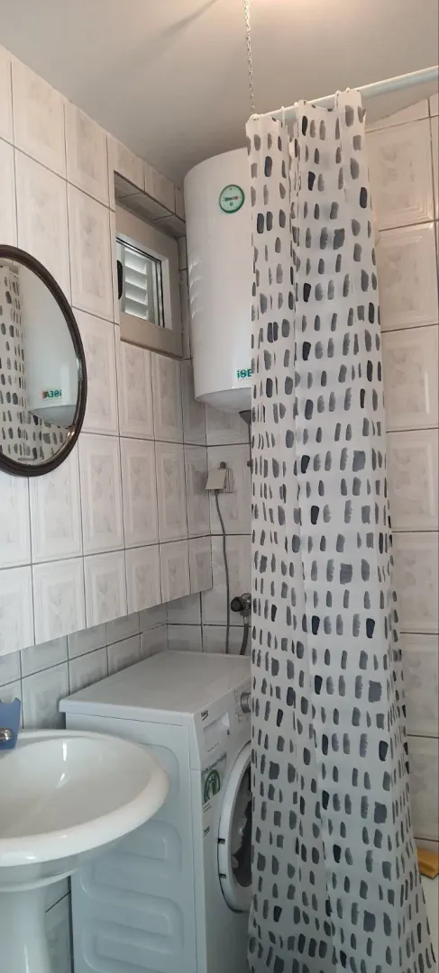 A simple bathroom featuring a washing machine, mirror, and a shower curtain.