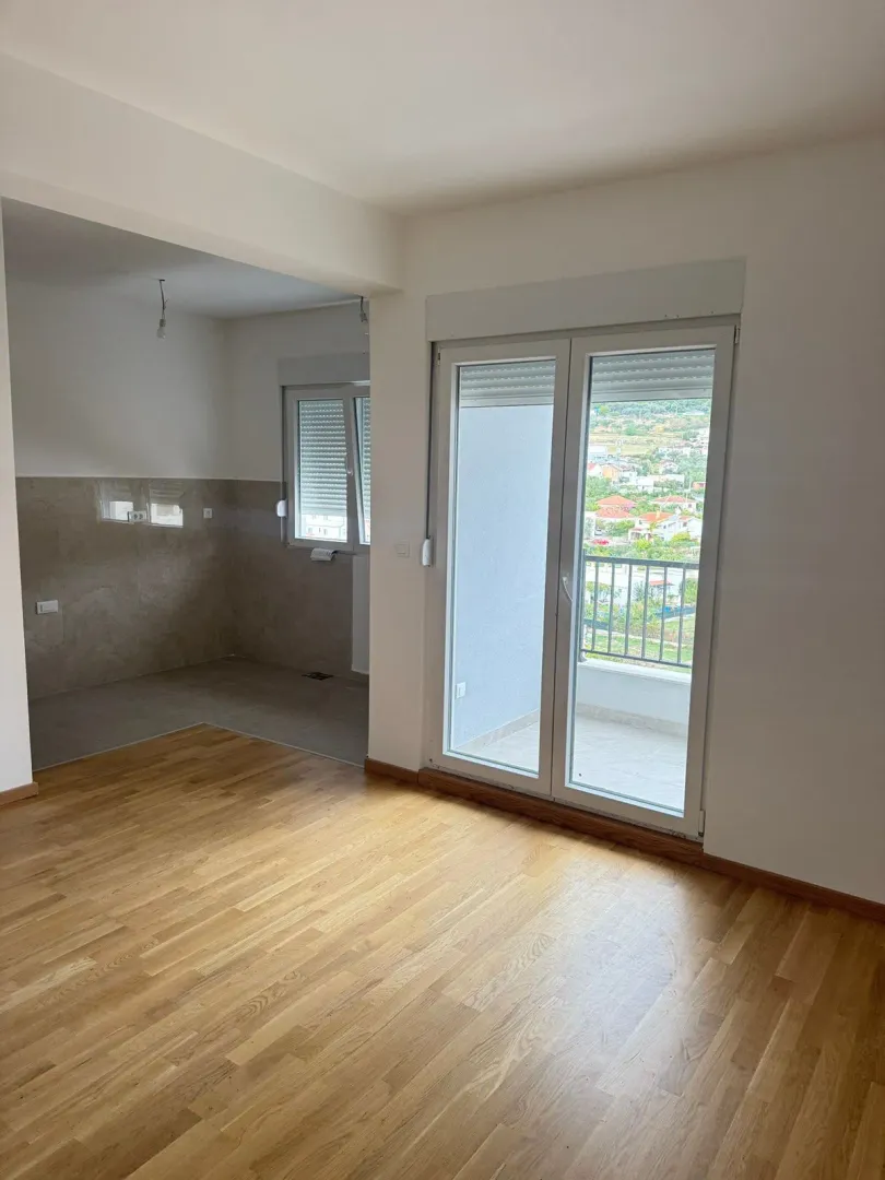 Empty living room with wooden flooring and access to the terrace.