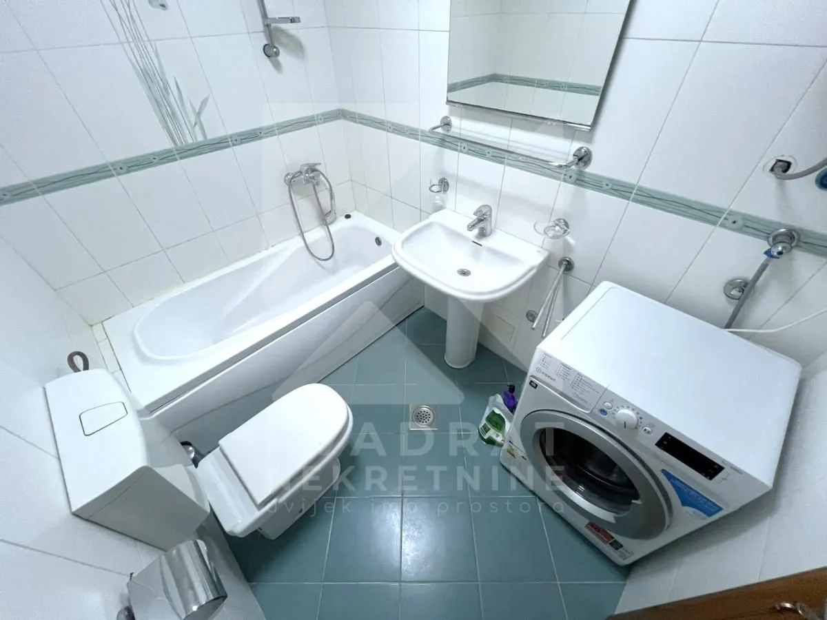 Kupatilo opremljeno kadom, umivaonikom, WC šoljom i veš mašinom.