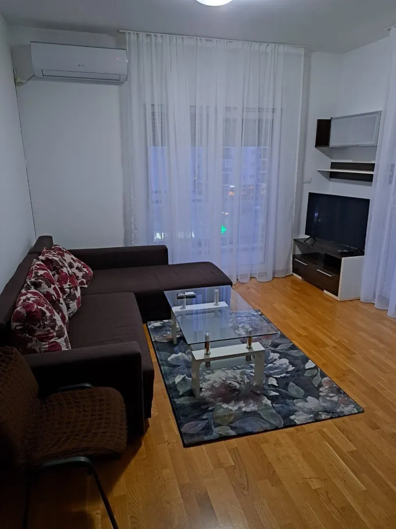 Svijetla dnevna soba sa ugaonom garniturom, staklenim stolom i televizorom.