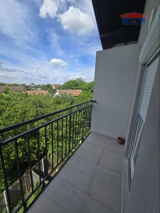 Manji popločani balkon sa crnom ogradom i pogledom na zelenilo i naselje.