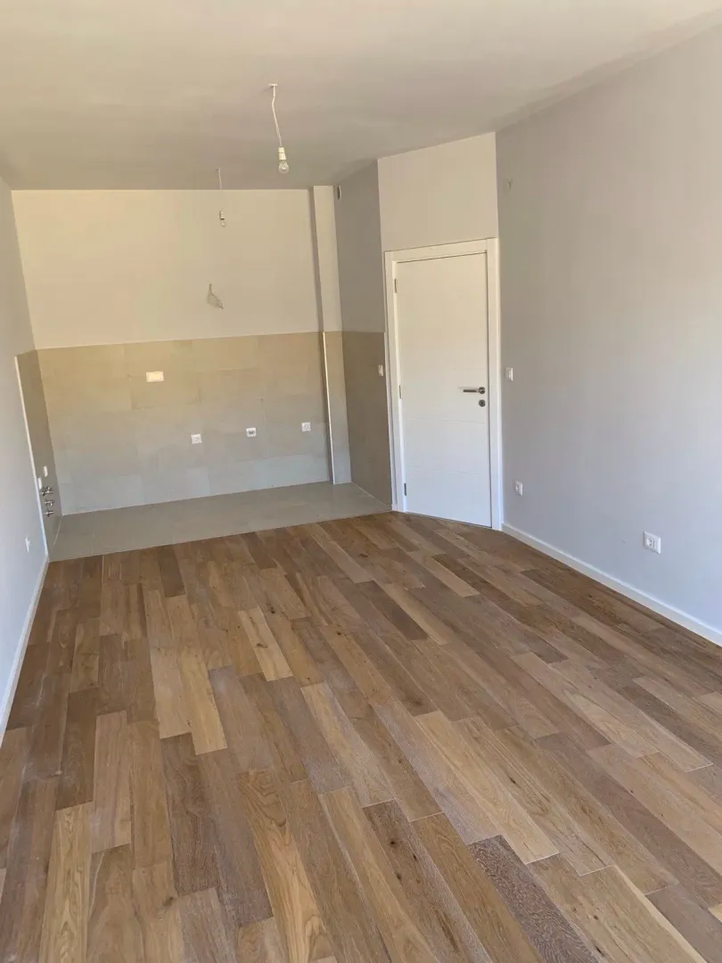 Unfurnished room with wooden flooring and wall tiles in the kitchen area.