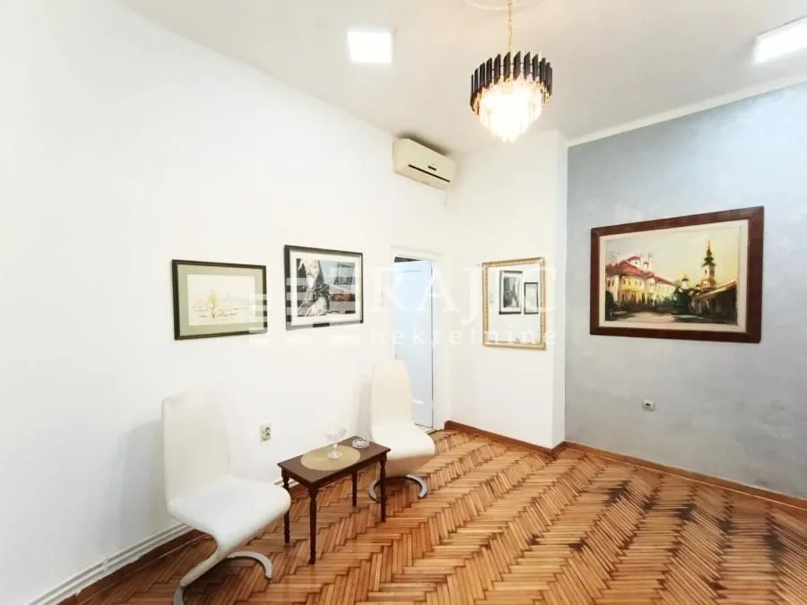 Living room with parquet flooring, furniture, and paintings on the wall.