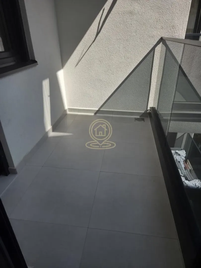 Prazan balkon sa staklenom ogradom i pločicama na podu.