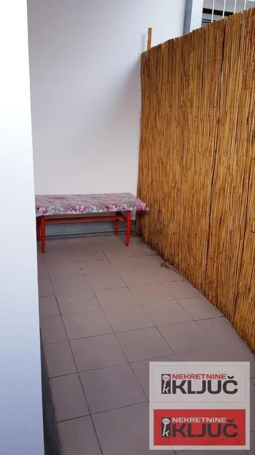 Natkriveni balkon sa popločanim podom i trpezarijskim stolom.